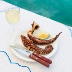 Grilled octopus and white wine glass on a table at the sea coast